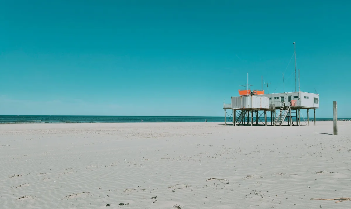 A building raised on tall pilings on an open sandy beach under a clear blue sky