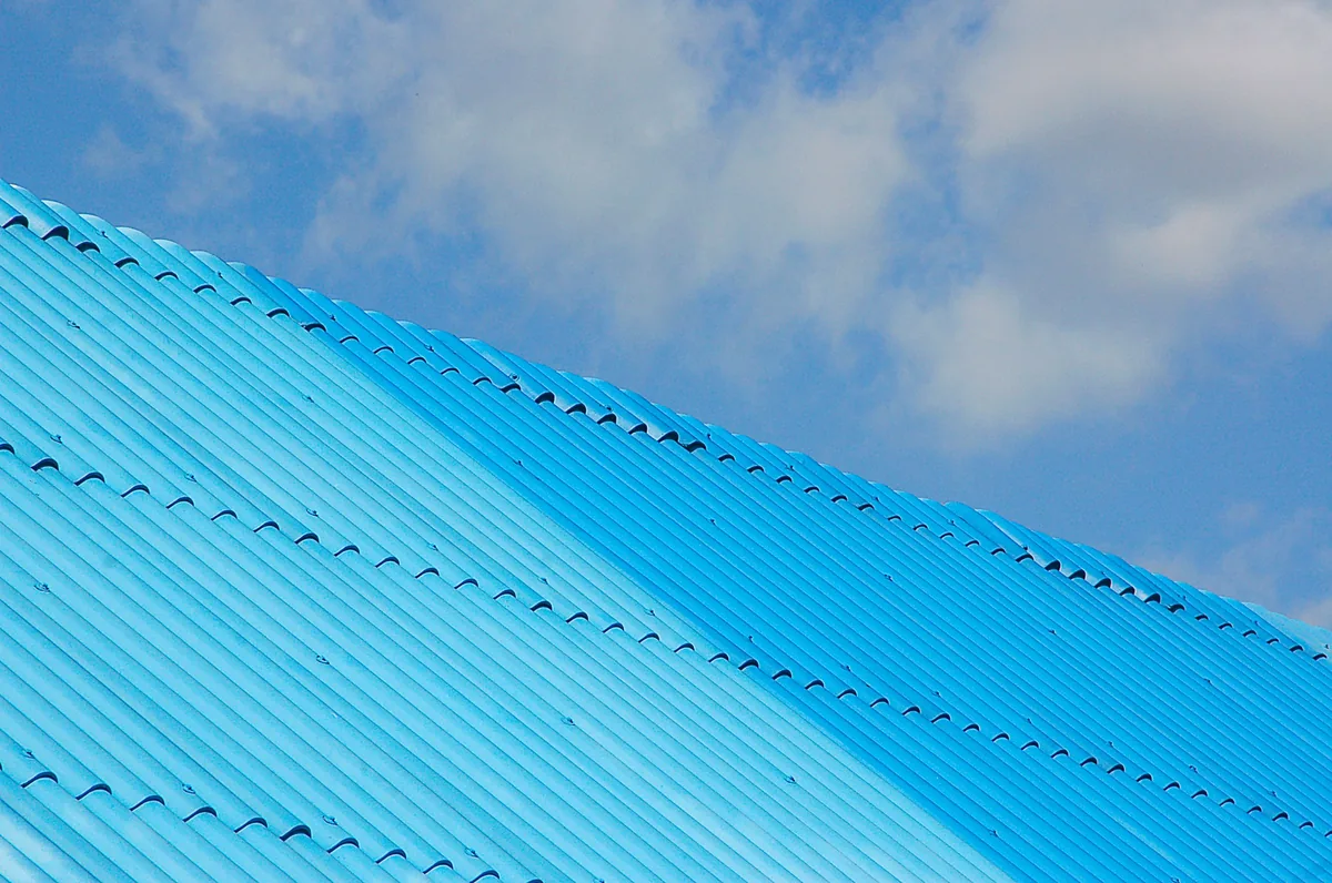 A blue corrugated metal roof angled against a blue sky with scattered clouds